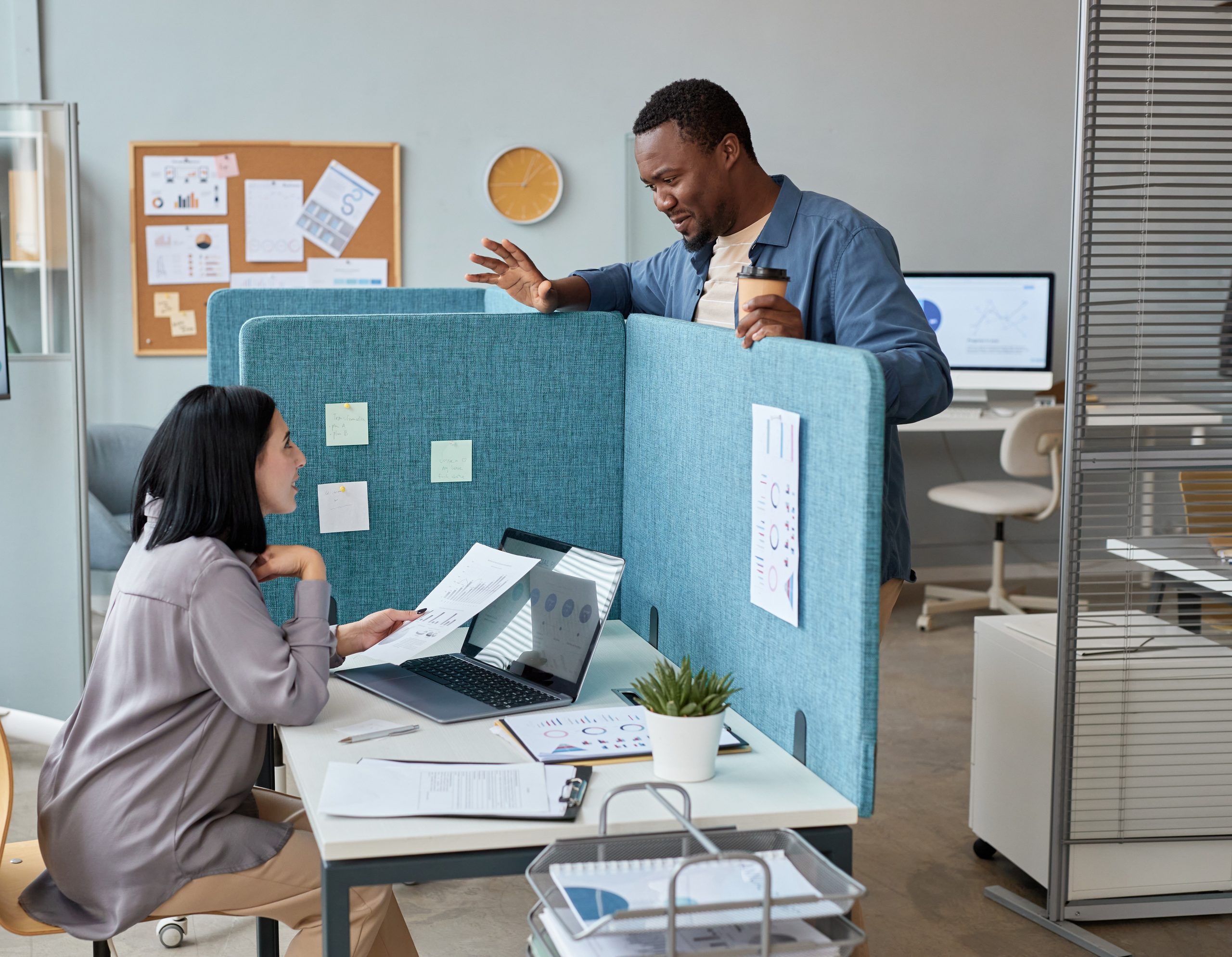 Two colleagues chatting in office over partition wall